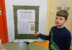 Chłopiec uczy się posługiwać bankomatem.